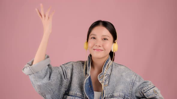 Happy pretty Asian teenager girl dancing and listening music by smartphone on pink background.