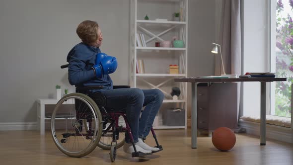 Young Depressed Boxer in Wheelchair Training Taking Off Boxing Gloves Holding Head in Hands