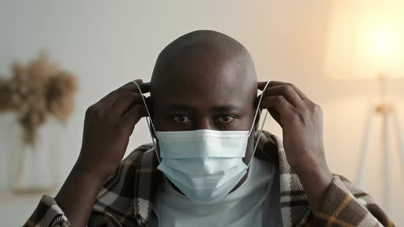 Portrait Of African Man Putting On Protective Face Mask Indoors
