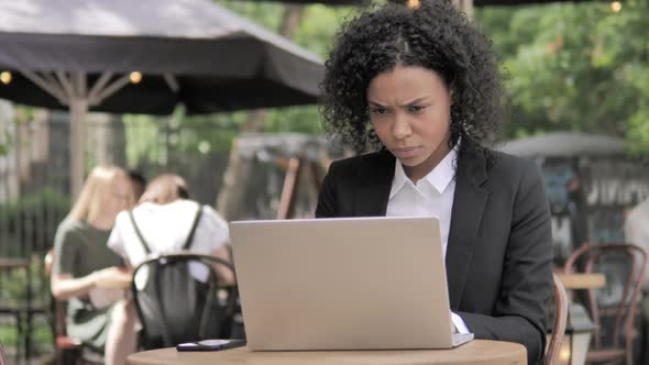 African Businesswoman in Shock By Results on Laptop in Outdoor Cafe