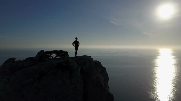 Aerial Silhouette of Young Woman Standing on the Top of a Mountain Facing the Sea