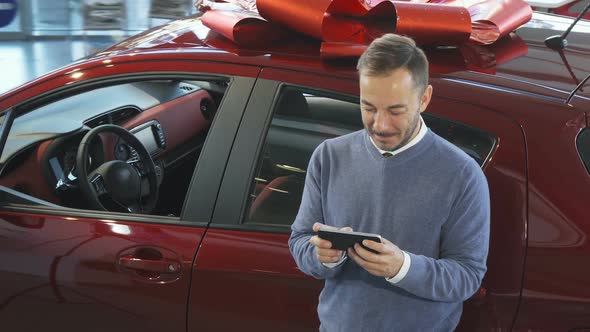 A Smiling Man Is Standing By the Car and Typing in the Phone