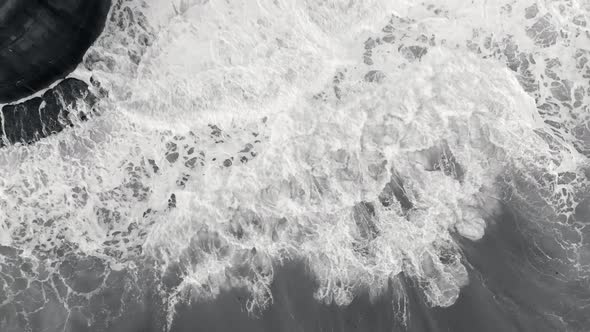Aerial footage of waves crashing against a sea wall in monochrome.