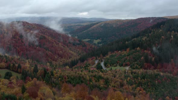 Flying over misty autumn forest with winding mountain road, Romania