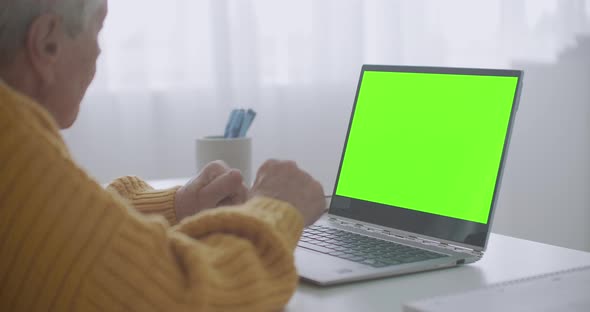 An Elderly Woman Looks at a Monitor with a Green Screen and Talks Via Video Link with Her