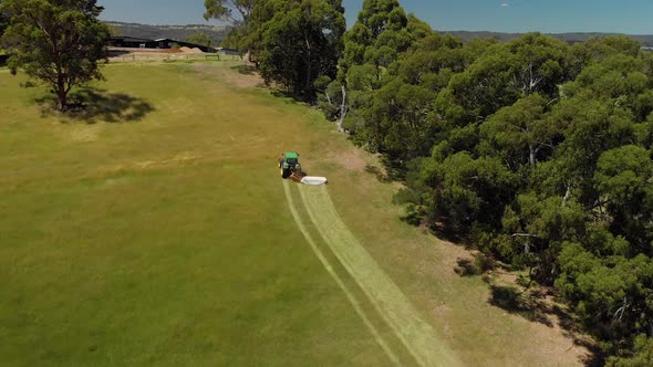 Aerial shot following a tractor slashing dry grass up a hill in rural Australia.