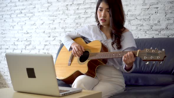 Young Asian Woman Practicing How to Play Guitar on Laptop