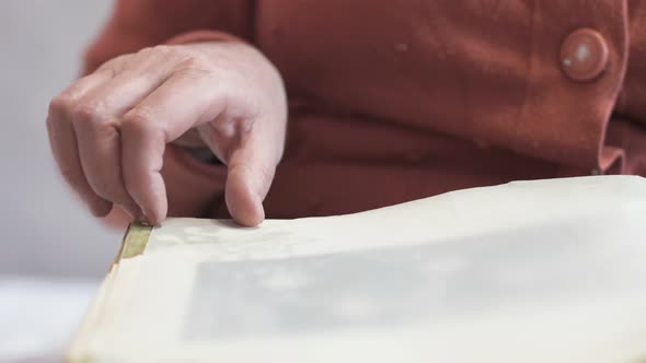 An elderly woman looks at photographs of an old photo album.