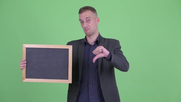 Stressed Businessman in Suit Holding Blackboard Giving Thumbs Down