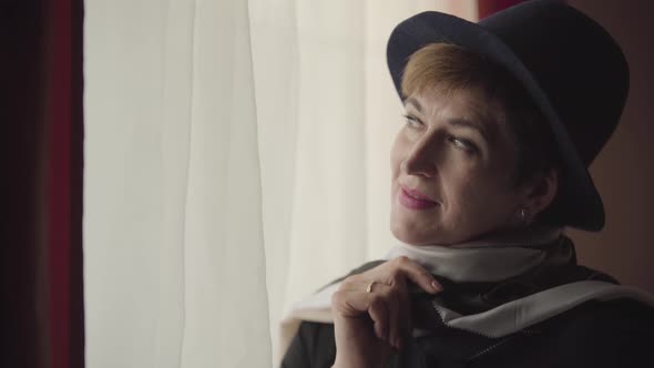 Close-up Face of Thoughtful Caucasian Woman in Stylish Hat and Scarf Looking Out the Window