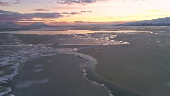 Flying over frozen lake during colorful sunset viewing ice