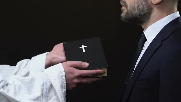 Priest Giving Business Man Holy Bible Against Black Background, Christianity