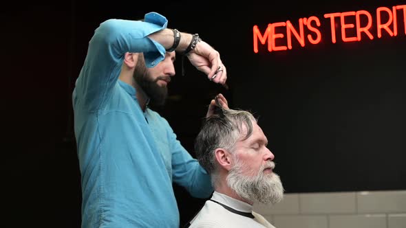 Barber gives a haircut to a gray-haired man in a barbershop