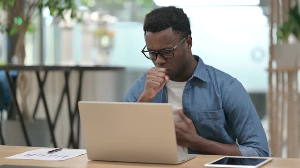 Young African Man Coughing While Using Laptop in Modern Office