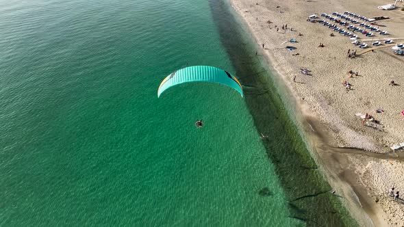 Aerial drone view of parachute jumper flying over beautiful beach