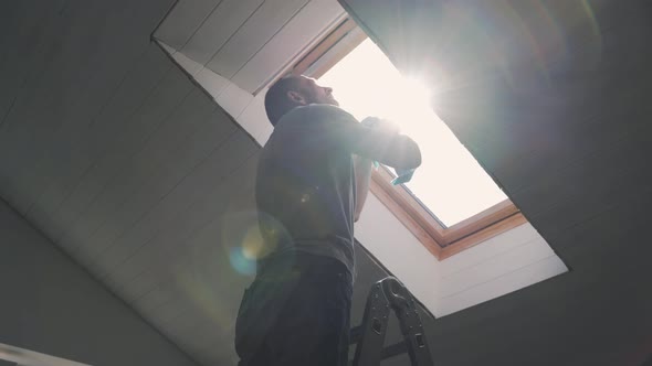 Caucasian Man Washes the Attic Window Bright Sun Illuminates the Man in the Window During the Repair