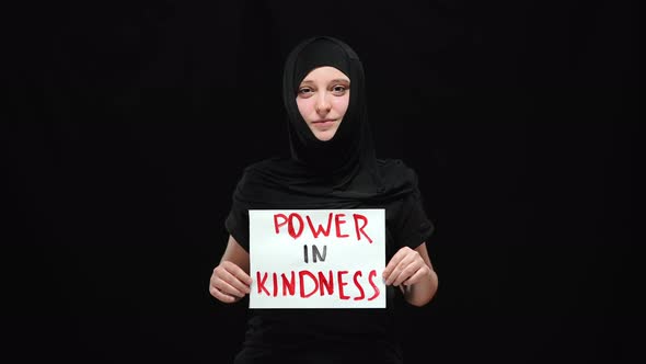 Portrait of Smiling Muslim Woman in Hijab Holding Power in Kindness Sign Looking at Camera