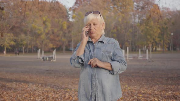 Mature European Woman Standing in the Autumn Park and Talking By Smart Phone. Positive Senior