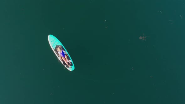 Young Blonde Woman Lying on Surfing Board Female Swimmer Wearing Swimming Suit Relaxing on Blue