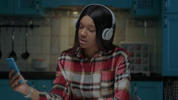 Young African American Woman Singing Songs Holding Mobile Phone in Hand Wearing White Headphones