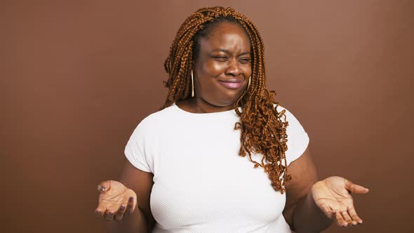 Emotional Incomprehensible Black Woman Shrugging Shoulders and Raising Hands Brown Background
