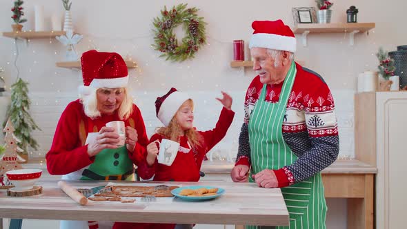 Senior Man with Cups Hot Chocolate Walking Into Christmas Home Kitchen to Grandmother and Grandchild