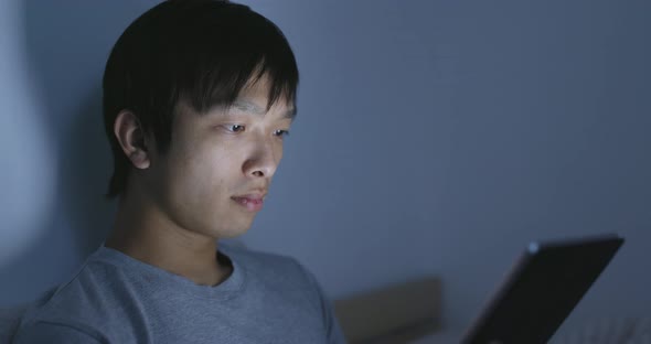 Asian man watching on tablet on bed 