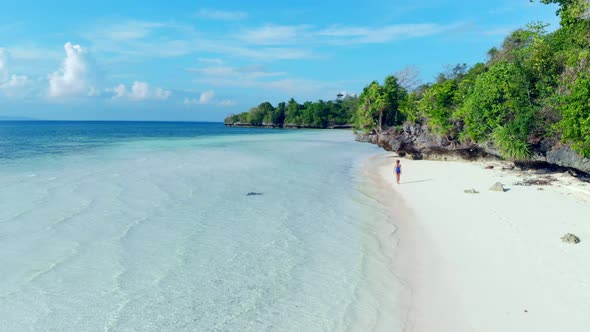 Aerial: woman walking on desert beach, tropical island white sand beach turquoise caribbean sea