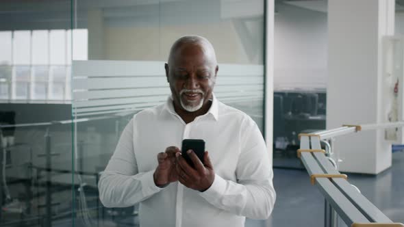 Smiling Mature Black Businessman Messaging On Smartphone While Walking In Business Center