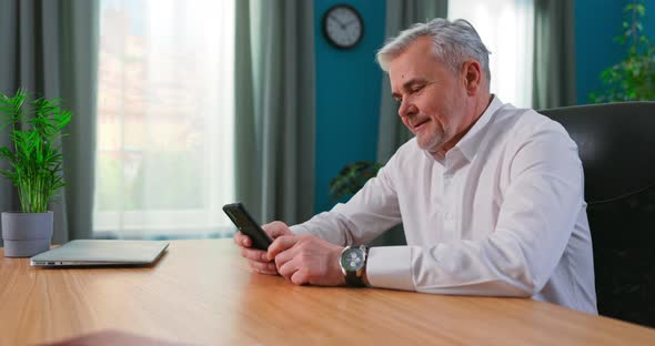 Middle Aged 55s Man Sitting Indoor Holding Mobile Phone Texting Sms Smiles Enjoy Easy Online