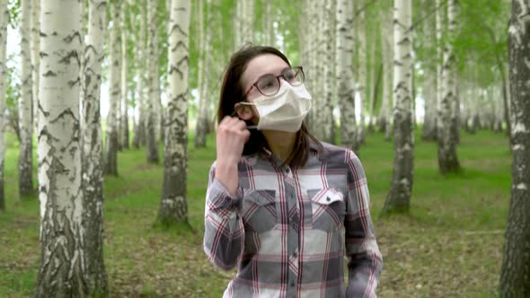 A Young Girl Takes Off a Medical Mask in the Forest. Happy Girl Walks in a Birch Forest. The End of