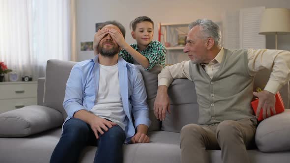 Grandfather and Schoolboy Congratulating Middle-Aged Man and Giving Red Gift Box