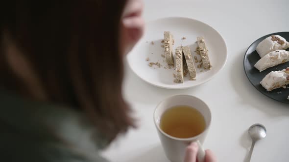 Young woman brunette tastes delicious halva slice holding white cup with tea. Breakfast