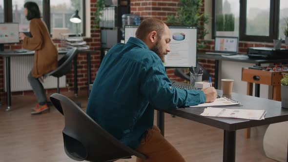 Man Taking Notes on Charts Papers and Looking at Computer