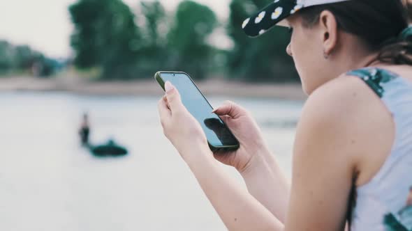 Beautiful Girl in a Bathing Suit Sits on a Sandy Beach with a Phone in Her Hands