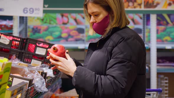 Woman in Mask Choice an Pomegranate in Her Hand in a Supermarket