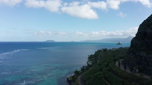 Aerial shot flying around the edge of a coastal mountain to reveal the Hawaiian coastline on O'ahu.