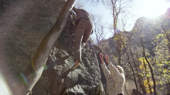 Man climbing boulder as woman holds arms up for safety