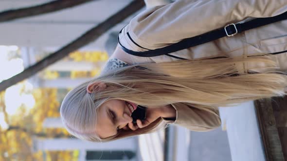 A Happy Young Girl Is Talking on a Mobile Phone in the Autumn Park of the City