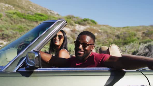 Portrait of african american couple waving and having fun while sitting in the convertible car on ro