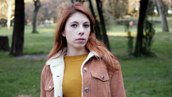 serious confident pretty red haired young woman staring at camera-outdoor