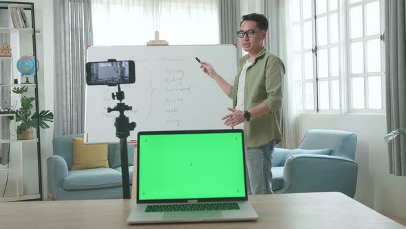 Asian Male Teacher With Green Screen Laptop Shoots Video By Smartphone Camera While Teaching English