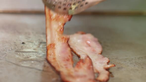 Close-up of bacon sizzling on a restaurant grill and flipped with tongs