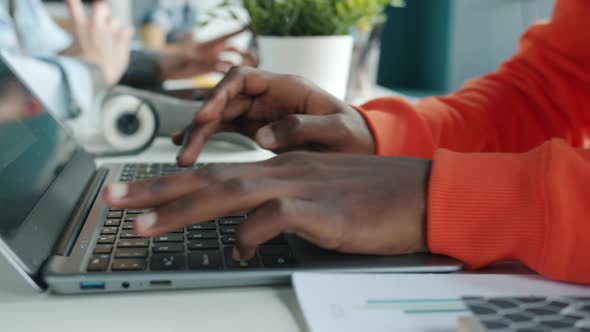 Closeup of Male Hands Typing with Laptop Indoors in Office While AfroAmerican Employee Working at