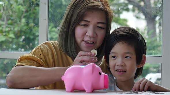 Cute Asian Child And Mother Putting A Coin In To A Piggy Bank