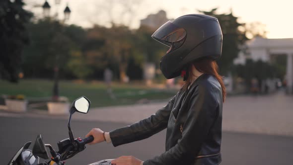 Beautiful Young Redhaired Woman Motorcyclist Sitting on Custom Bike with Black Motorcycle Helmet