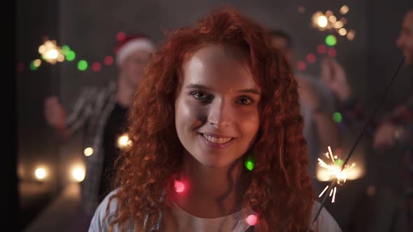Cheerful Curly Redhaired Girl with Colorful Lights on Neck Posing for Camera Smiling Holding Her