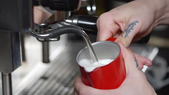 Barista Steaming Milk in Red Pitcher on Coffee Machine