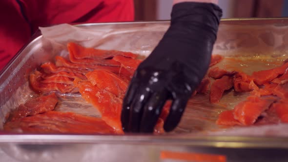 Palm Hands in Black Gloves Take Sliced Red Salmon Fish From Metal Container