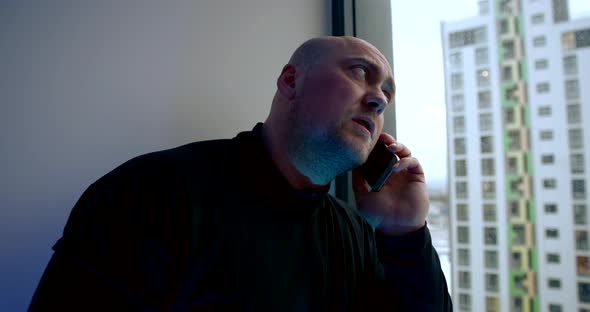 Middle-aged Man Is Talking By Cell Phone Indoors, Looking at Window